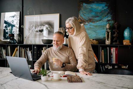 a man and a woman sitting at a table using a laptop talking